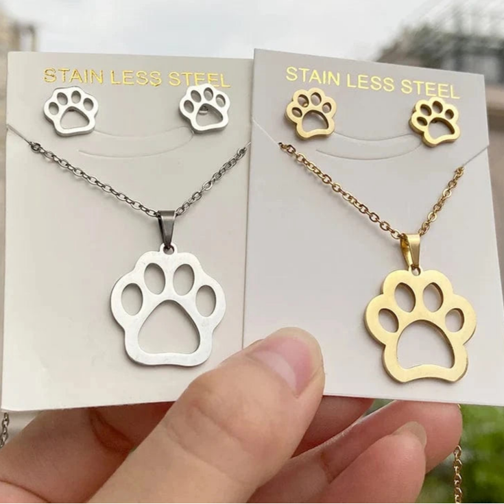 Gold and silver paw print necklaces on branded card held by a hand.