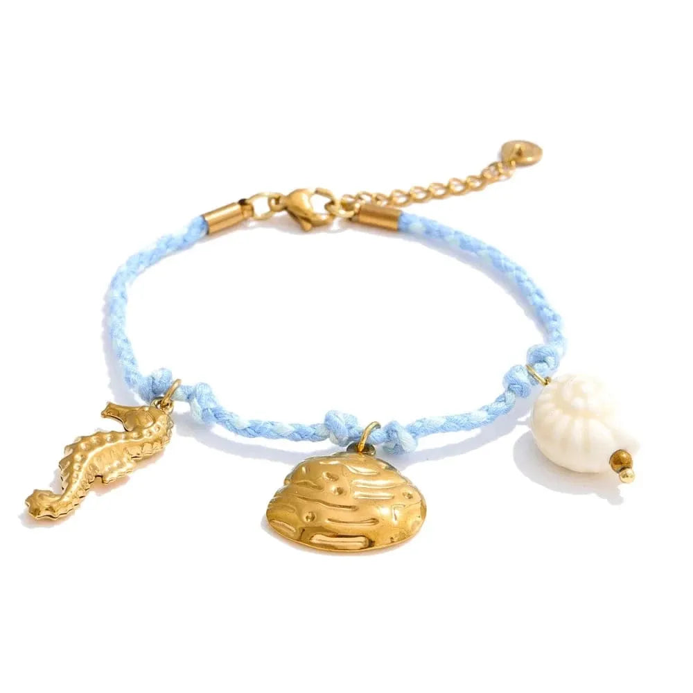 Bracelet with gold charms including a seahorse, shell, and pearl on a light blue cord.
