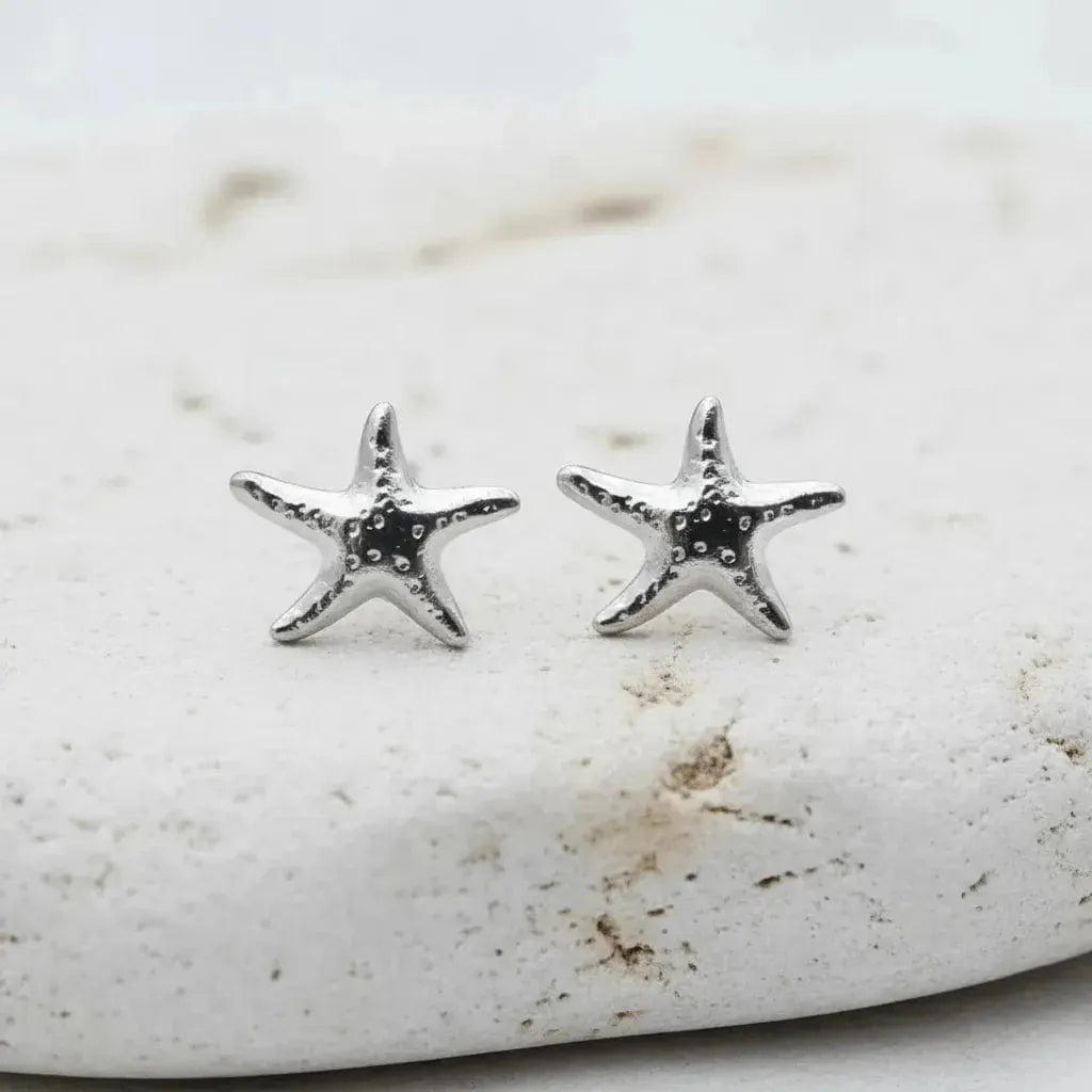 Silver starfish earrings on a textured stone surface
