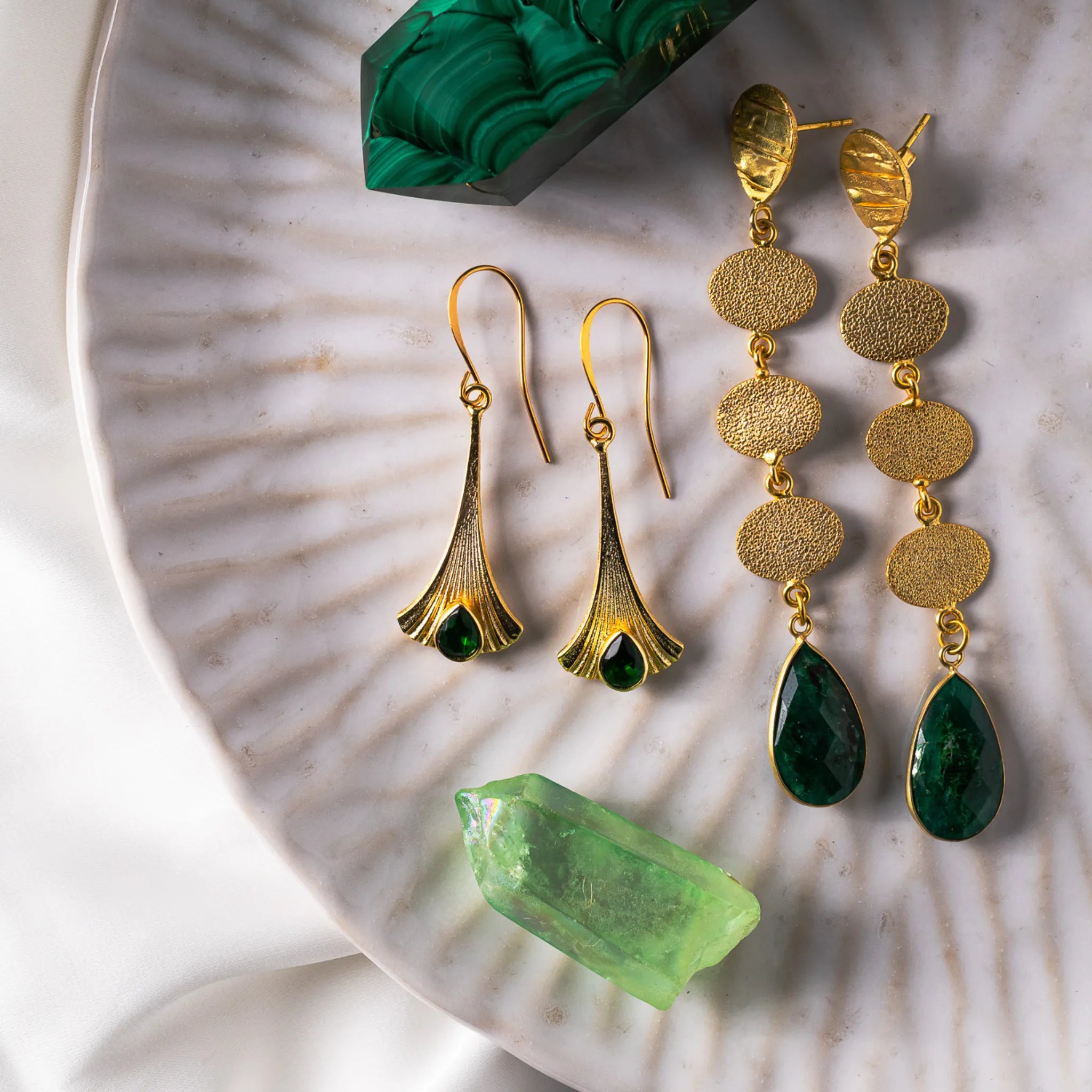 Statement earrings featuring cascading gold-plated sterling silver discs and teardrop-shaped opaque emerald stones, symbolizing growth and renewal.