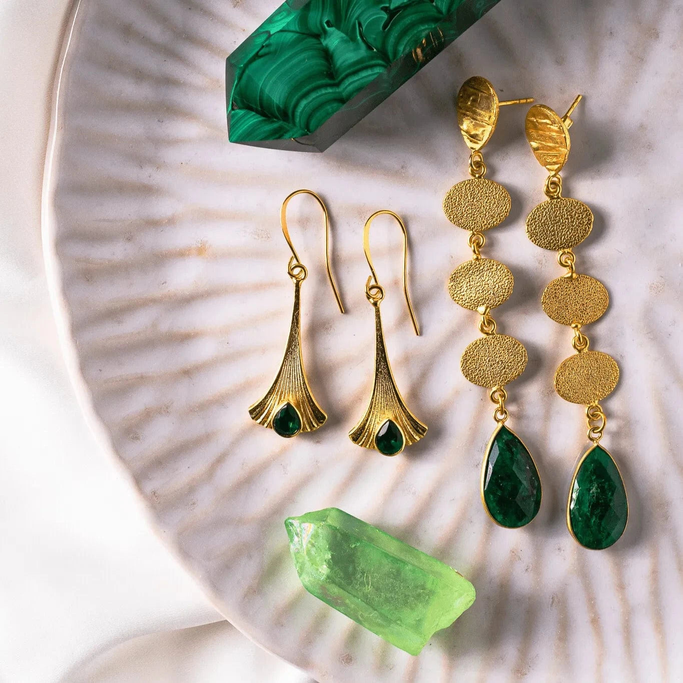 Statement earrings featuring cascading gold-plated sterling silver discs and teardrop-shaped opaque emerald stones, symbolizing growth and renewal.