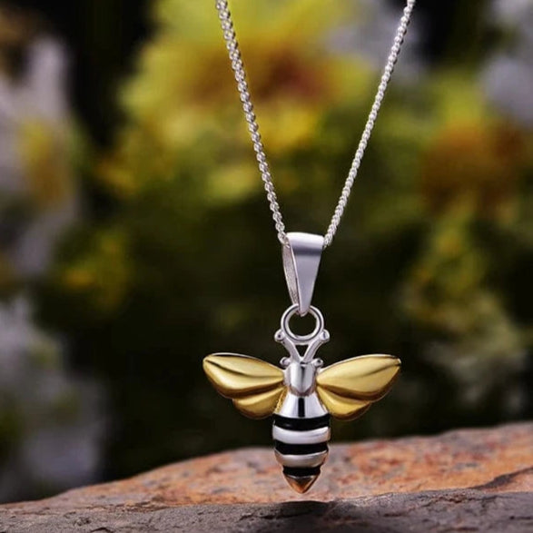 Bee-shaped pendant necklace on a stone surface with a blurred floral background