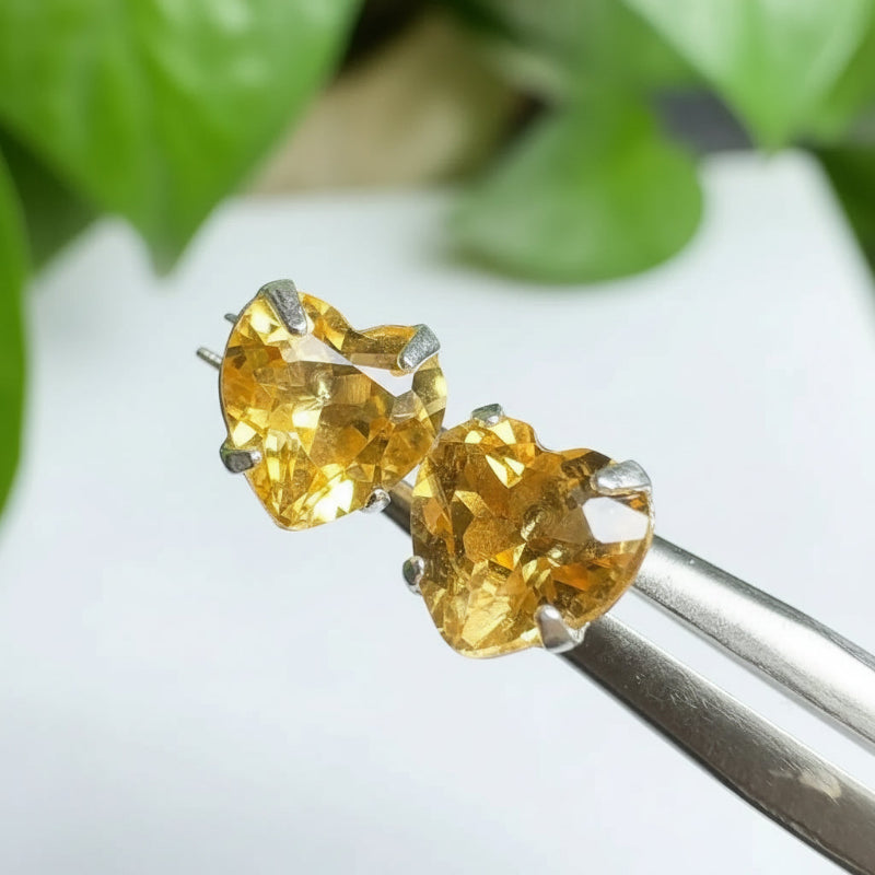 Pair of yellow gemstone earrings held by tweezers with a green leafy background
