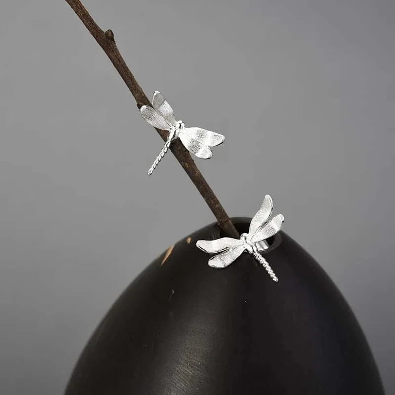 Silver dragonfly earrings on a branch against a gray background