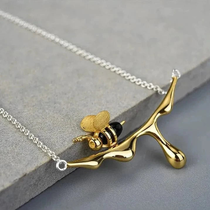 Gold branch-shaped pendant with a bee on a silver chain against a gray stone background