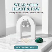 Silver paw print earrings on a white stand with text about animal rescue and a green crystal.