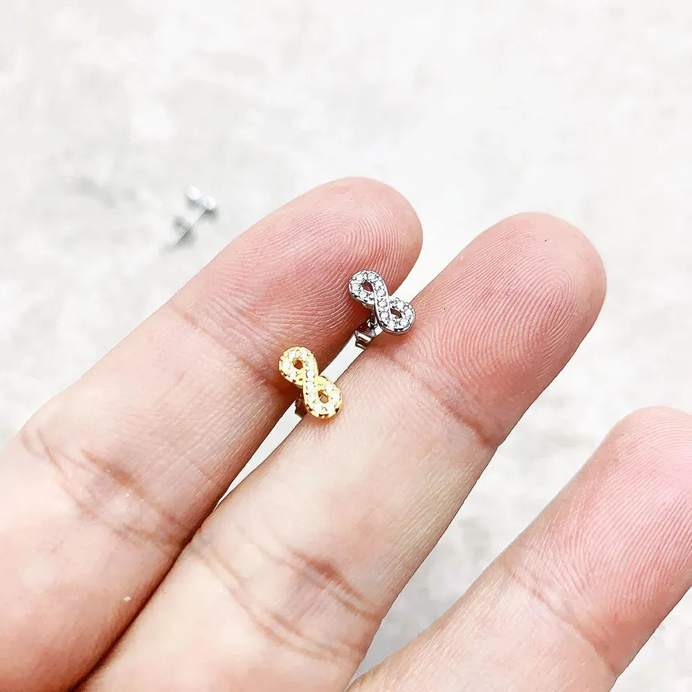 Two earrings, one gold and one silver, held between fingers against a light background.