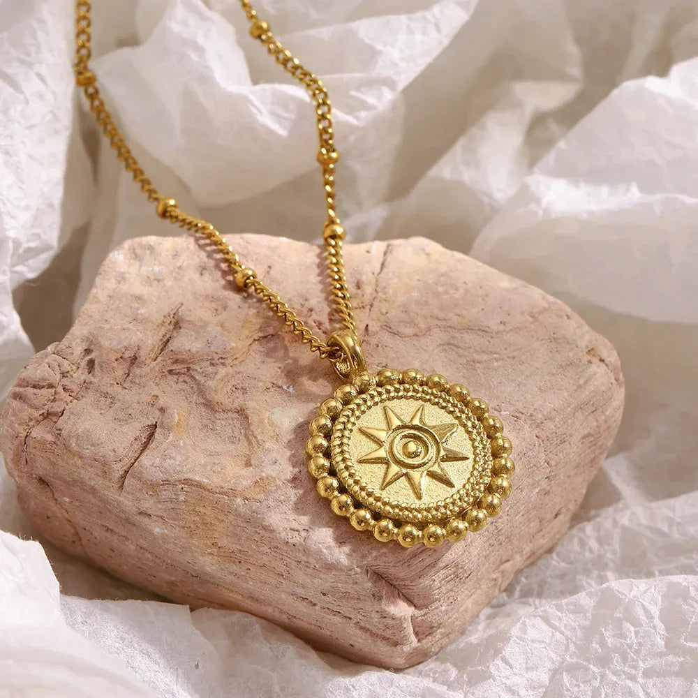 Hammered gold sun medallion pendant necklace on curb chain, styled on sandstone  