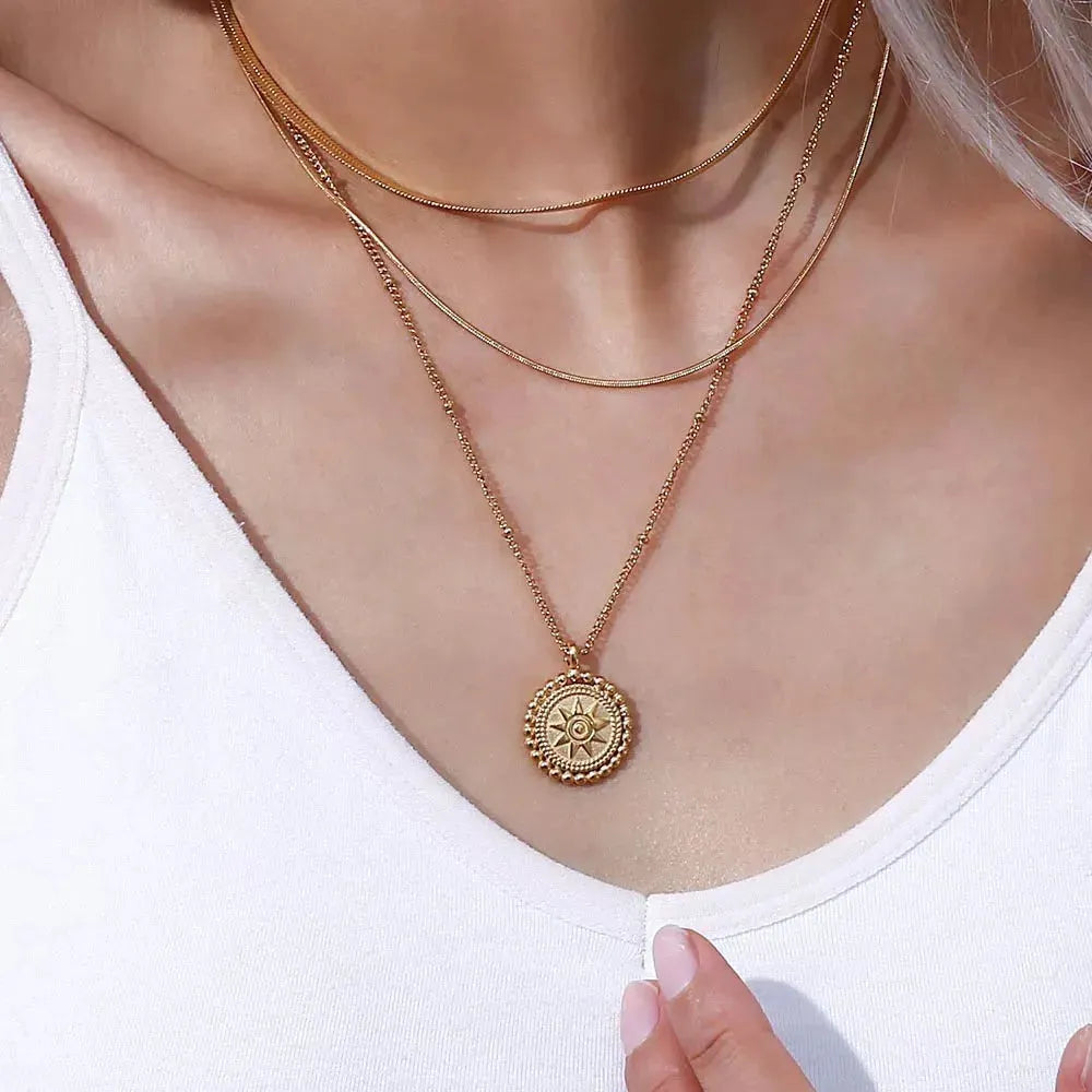 Hammered gold sun medallion pendant necklace on curb chain, styled on sandstone  