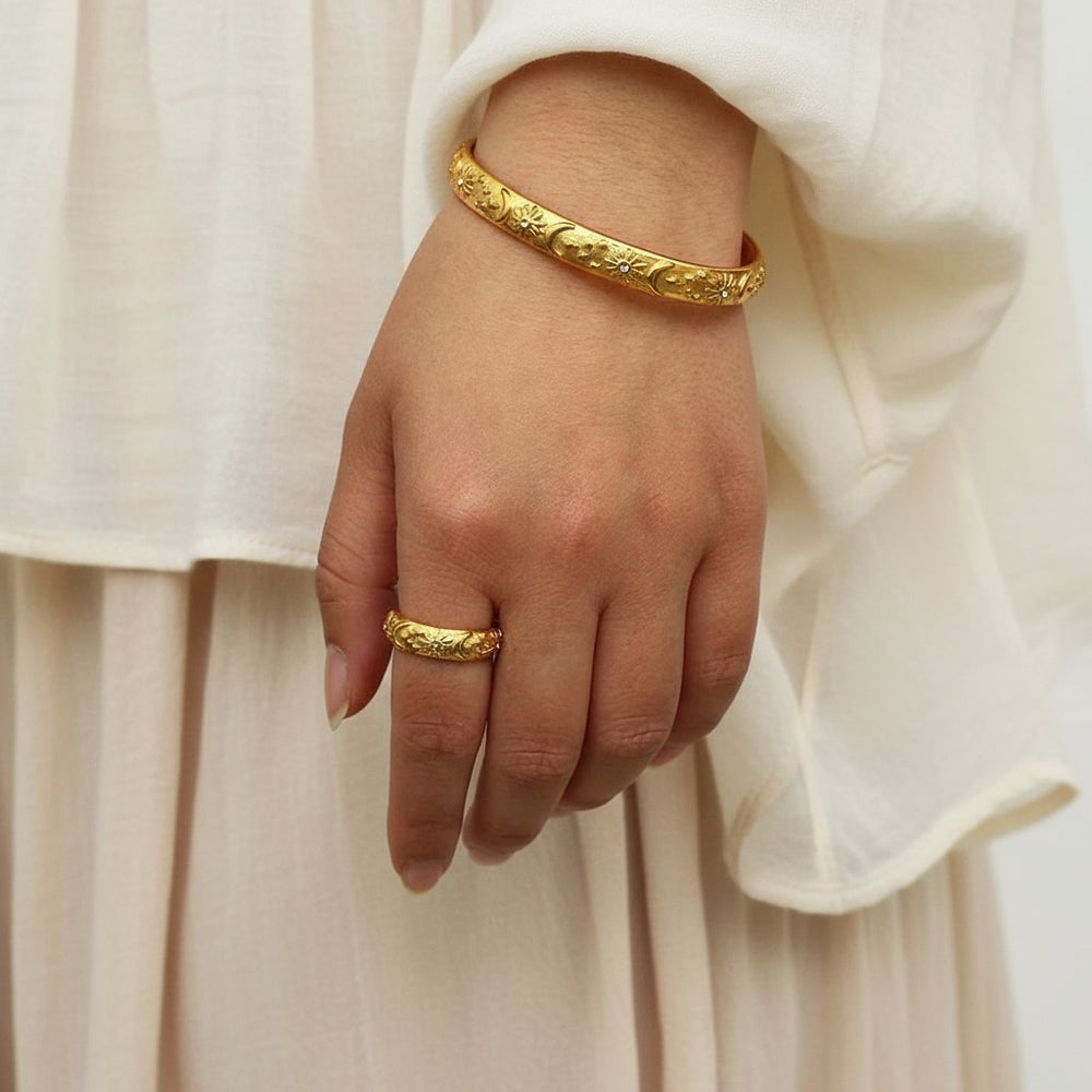 Hand wearing a gold bracelet and ring with a blurred background