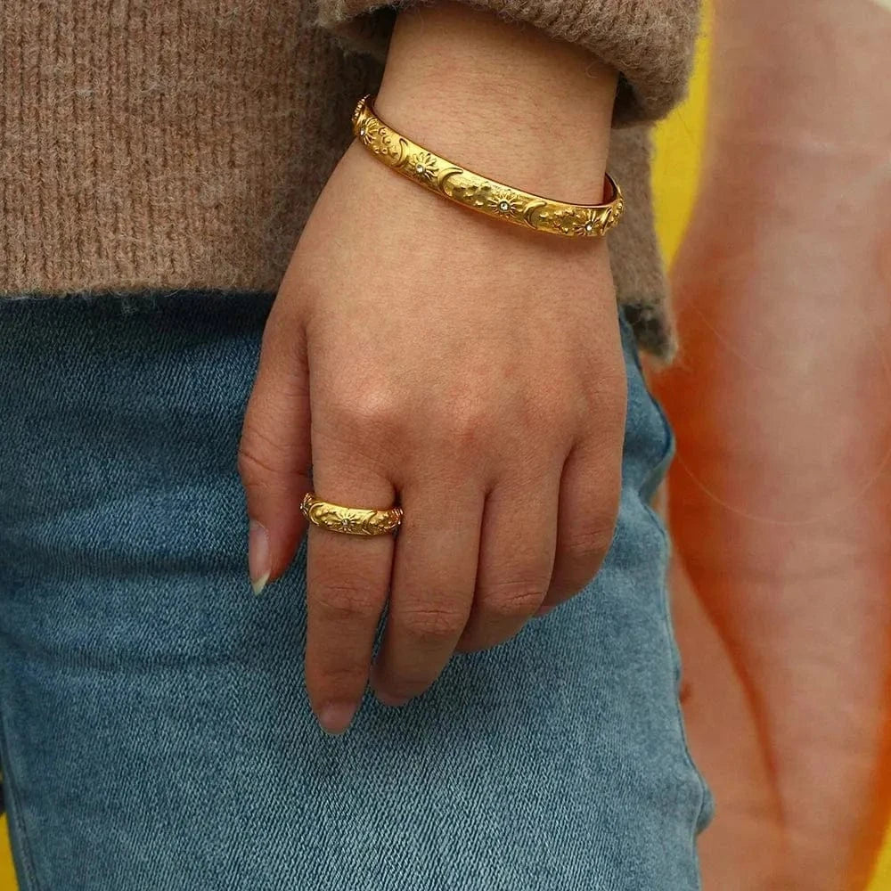 Hand wearing a gold bracelet and ring with a blurred background