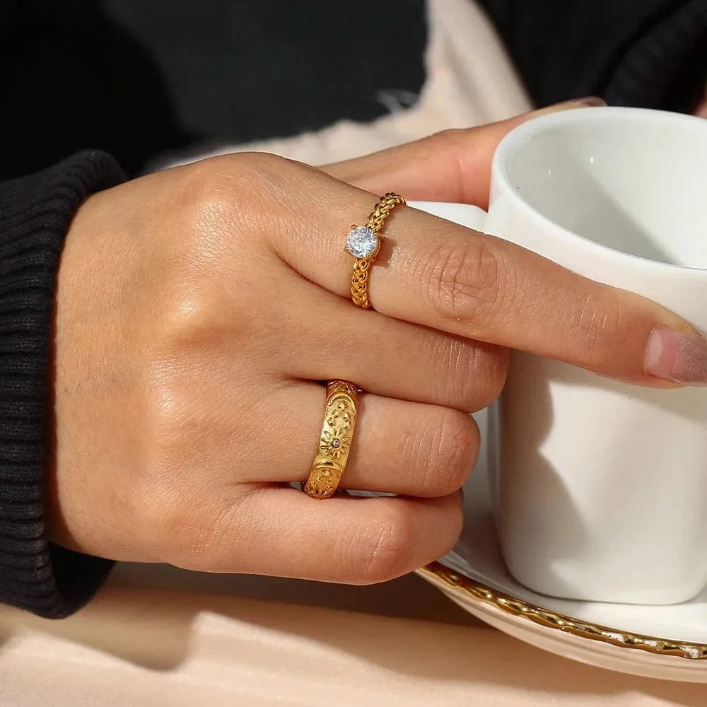 Hand wearing two gold rings holding a white cup with a gold handle.