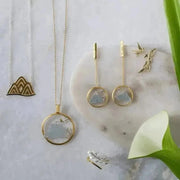 Gold jewelry set including necklaces, earrings, and rings on a marble surface with green leaves.