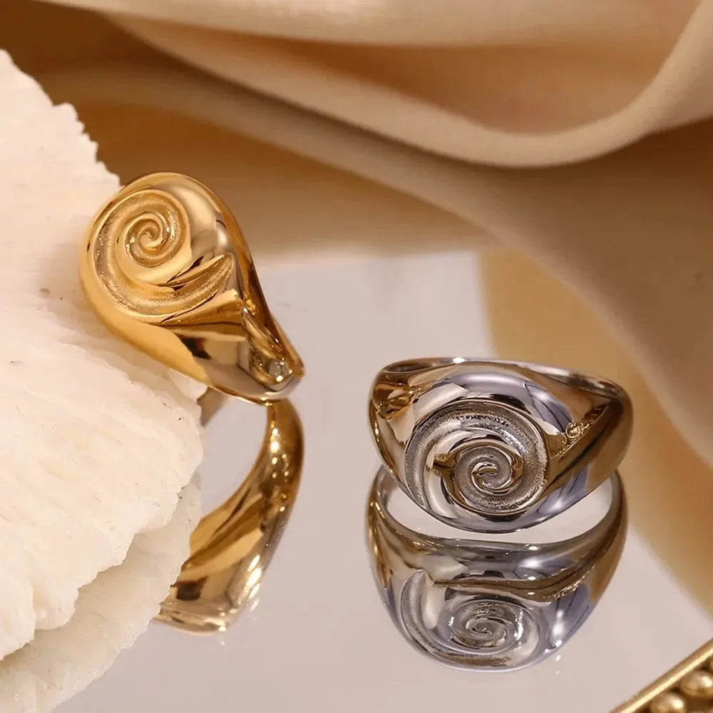 Gold and silver rings with spiral designs on a beige fabric background