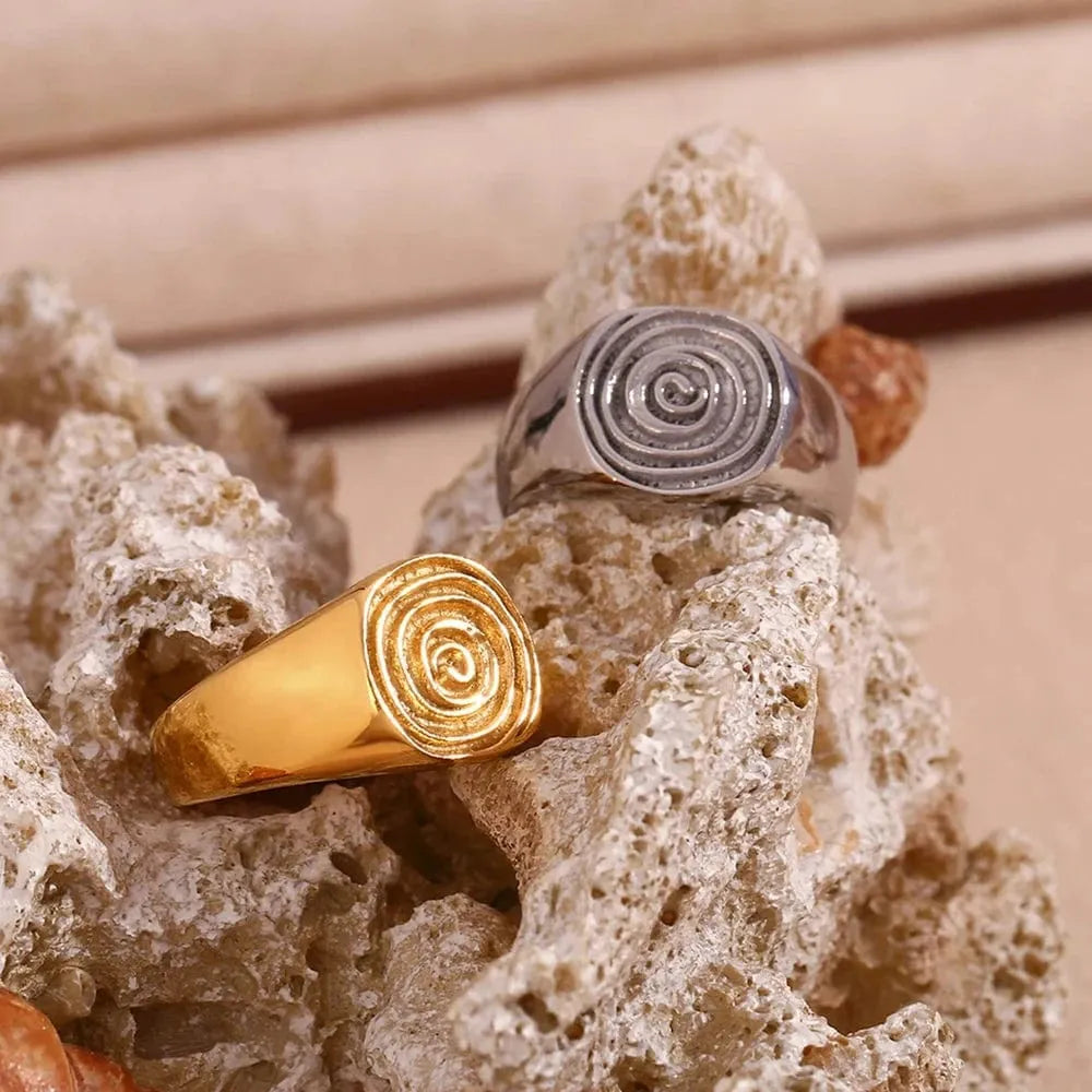 Two spiral-patterned rings, one gold and one silver, on a textured surface.