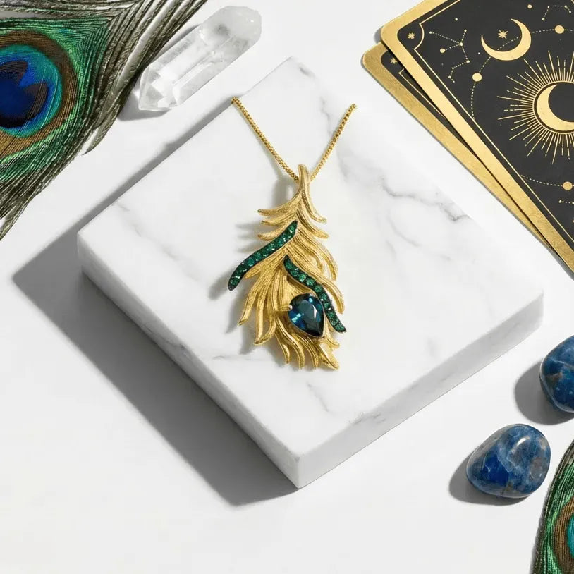Gold feather necklace with blue stones on a white marble surface with peacock feathers and tarot cards.
