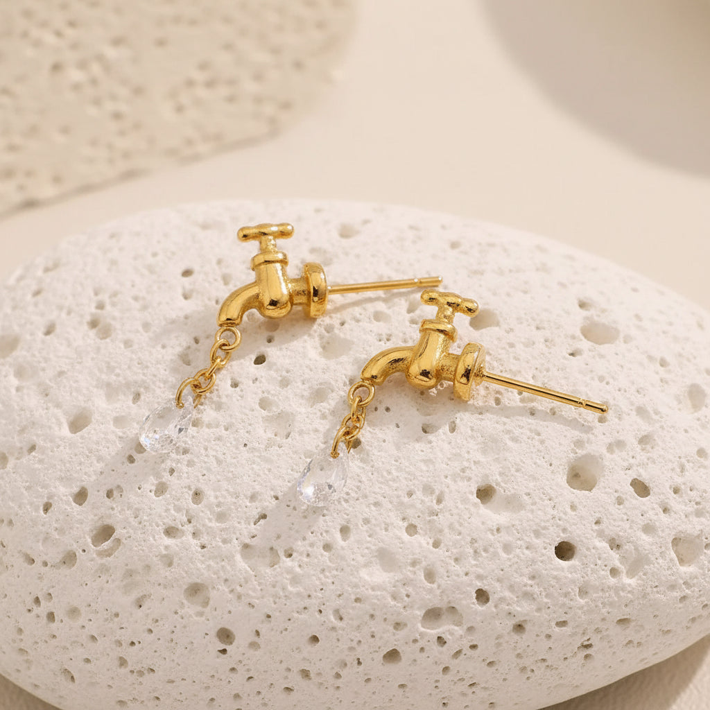 Gold earrings with water faucet design on a textured stone surface