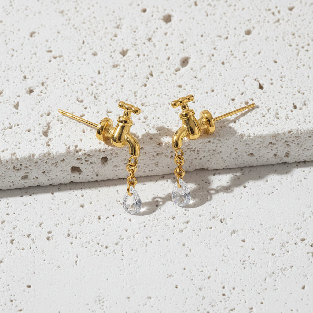 Gold faucet-shaped earrings with a chain and pearl drop on a white background