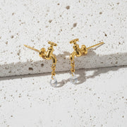 Gold faucet-shaped earrings with a chain and pearl drop on a white background