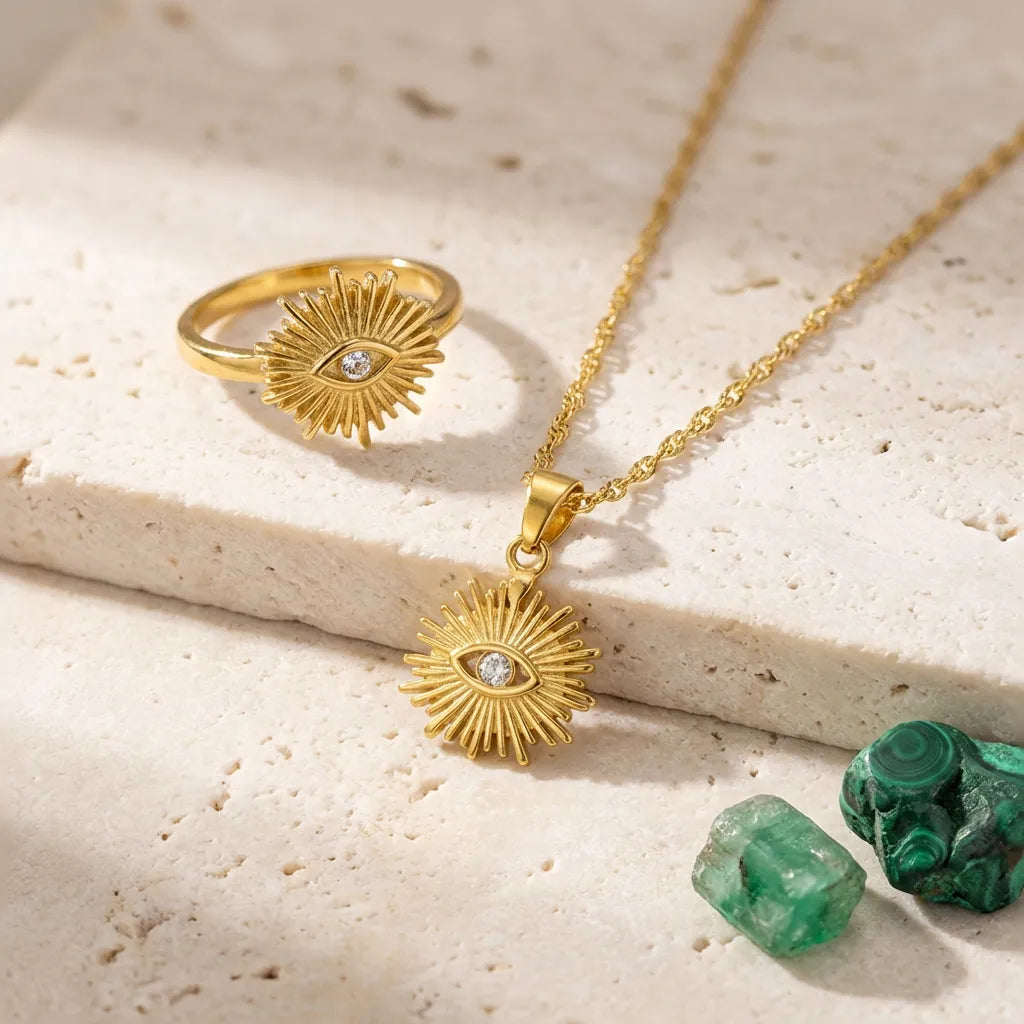 Gold ring and necklace with eye design on a beige surface with green stones.