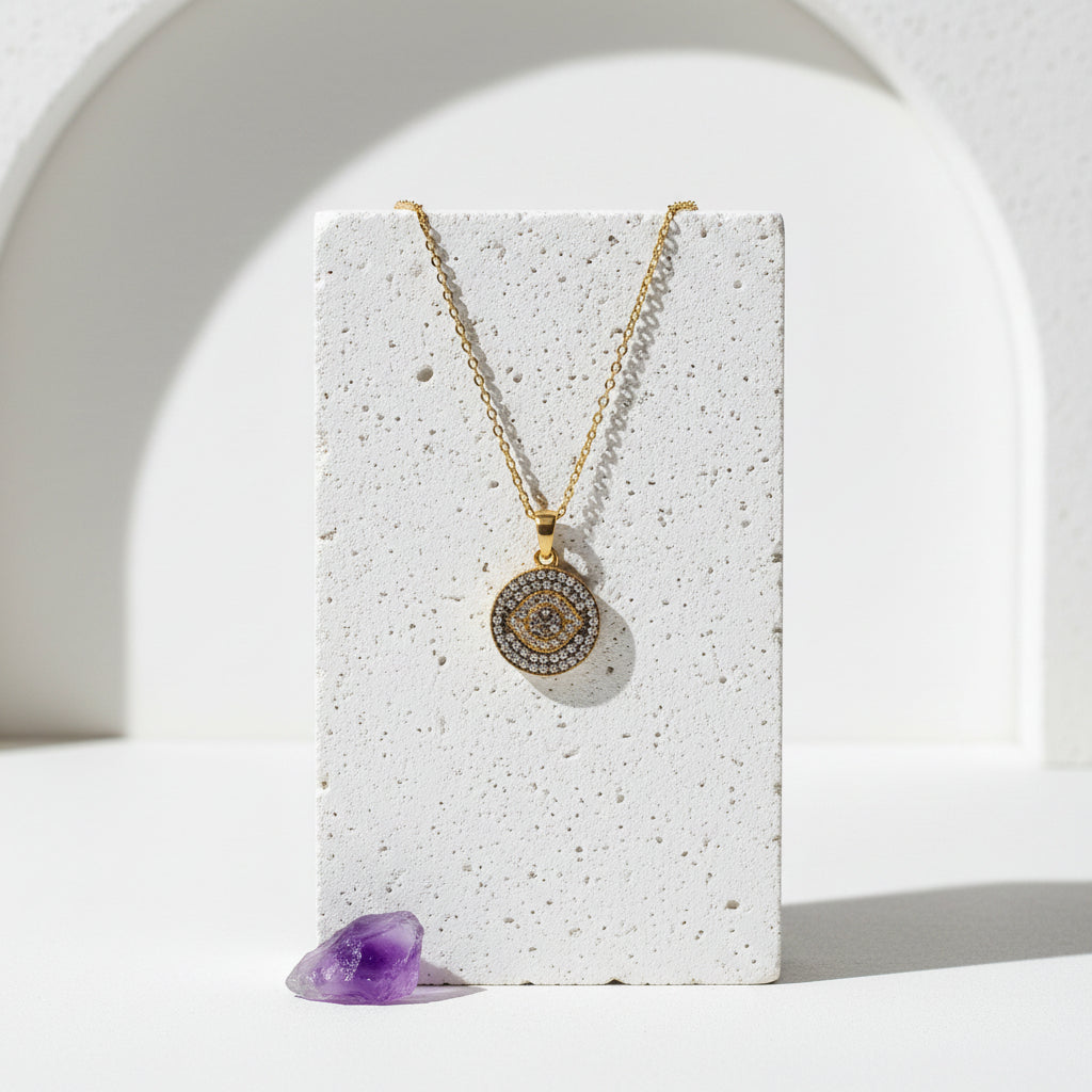 Gold third eye pavé necklace, cubic zirconia rays set around a round pendant, laid on pale stone with amethyst.