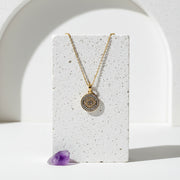 Gold third eye pavé necklace, cubic zirconia rays set around a round pendant, laid on pale stone with amethyst.