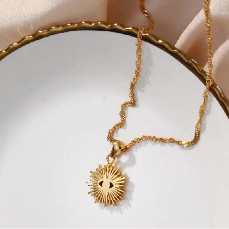 Gold necklace with a sun-shaped pendant on a white plate and beige fabric background