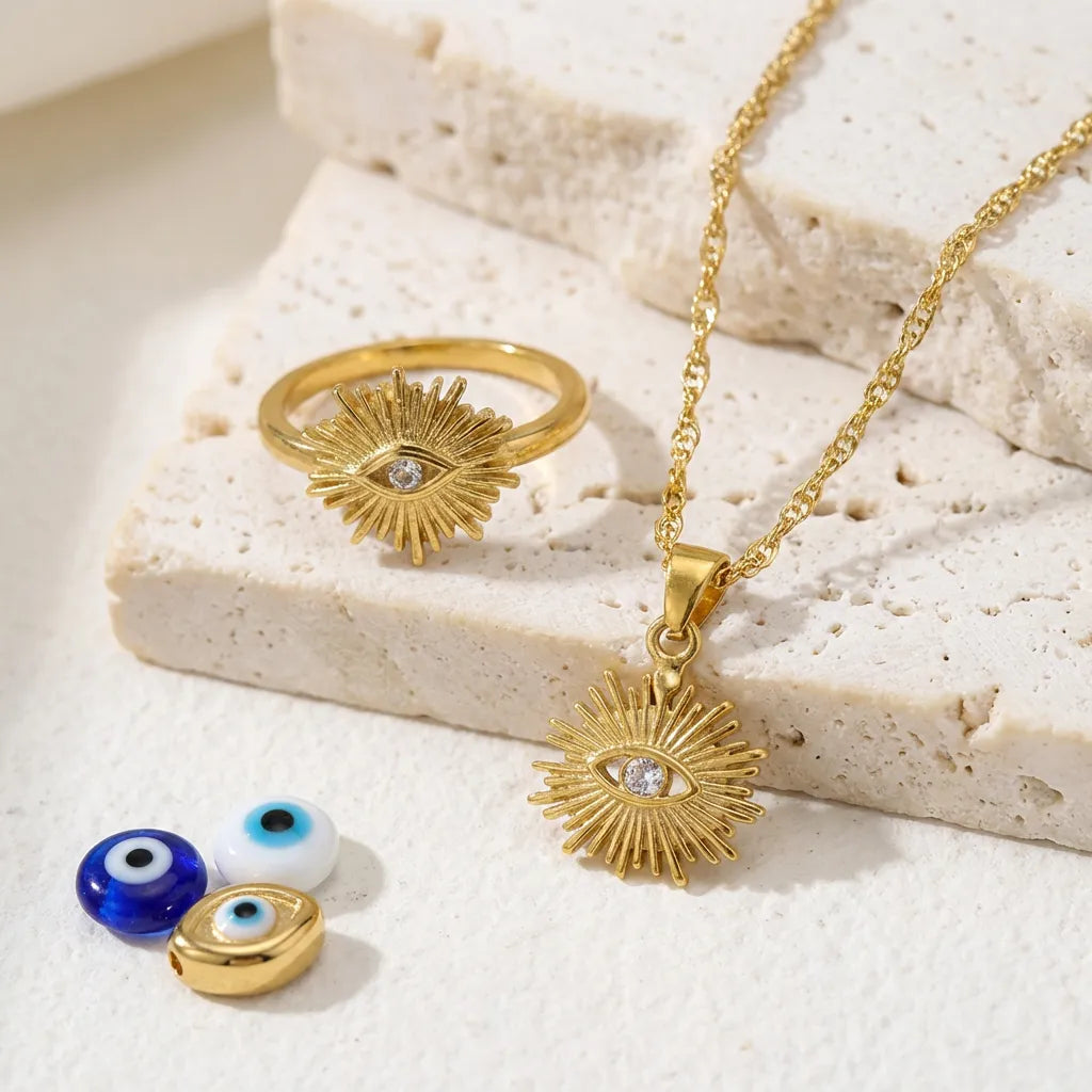 Gold jewelry set with ring, necklace, and small evil eye pendants on a textured surface