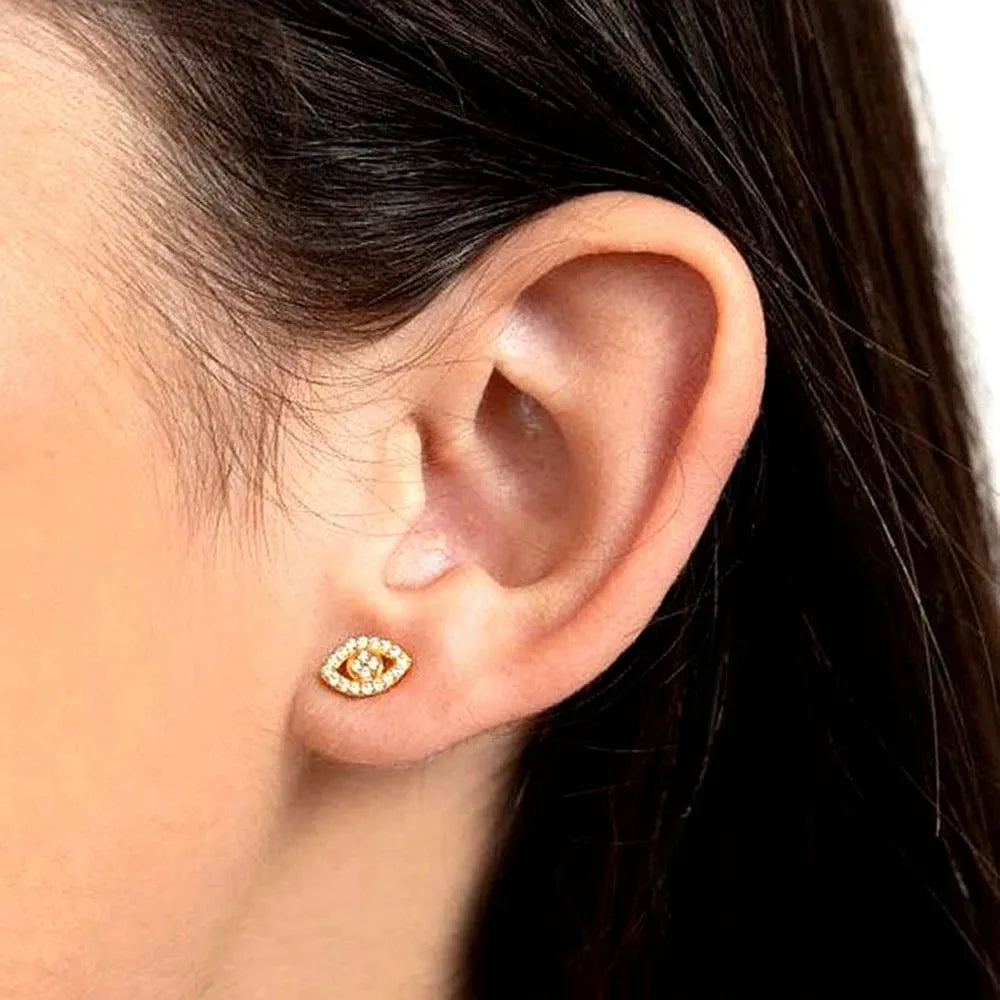 Gold earring worn on a person's ear with a neutral background