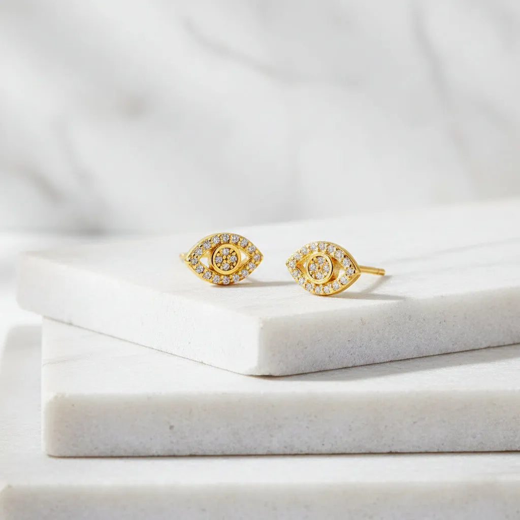 Gold eye-shaped earrings with clear stones on a white background