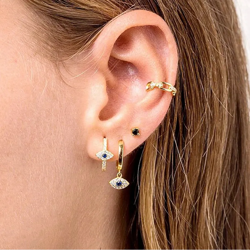 Close-up of an ear with multiple gold earrings on a plain background