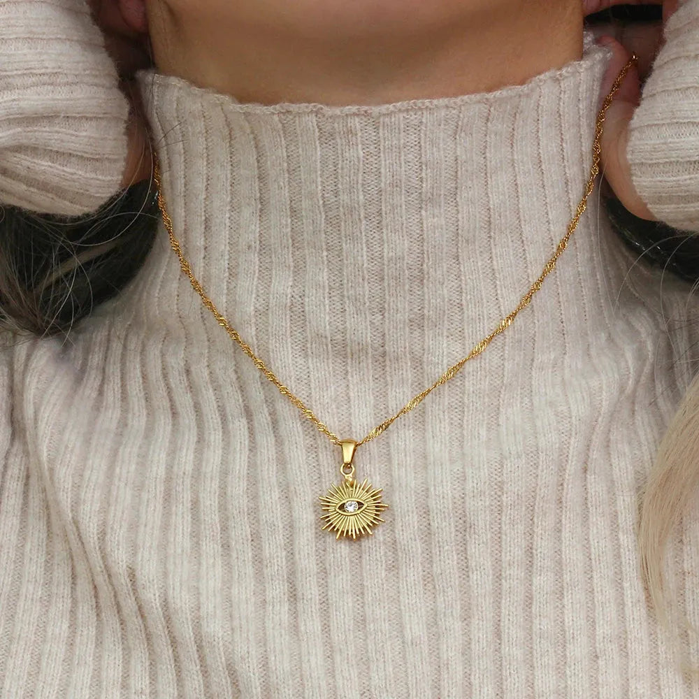 Gold necklace with a pendant worn by a person in a beige sweater.