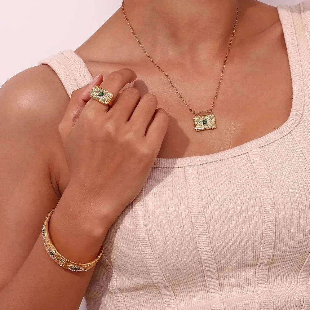 Close-up of a person wearing a gold necklace, ring, and bracelet on a light background