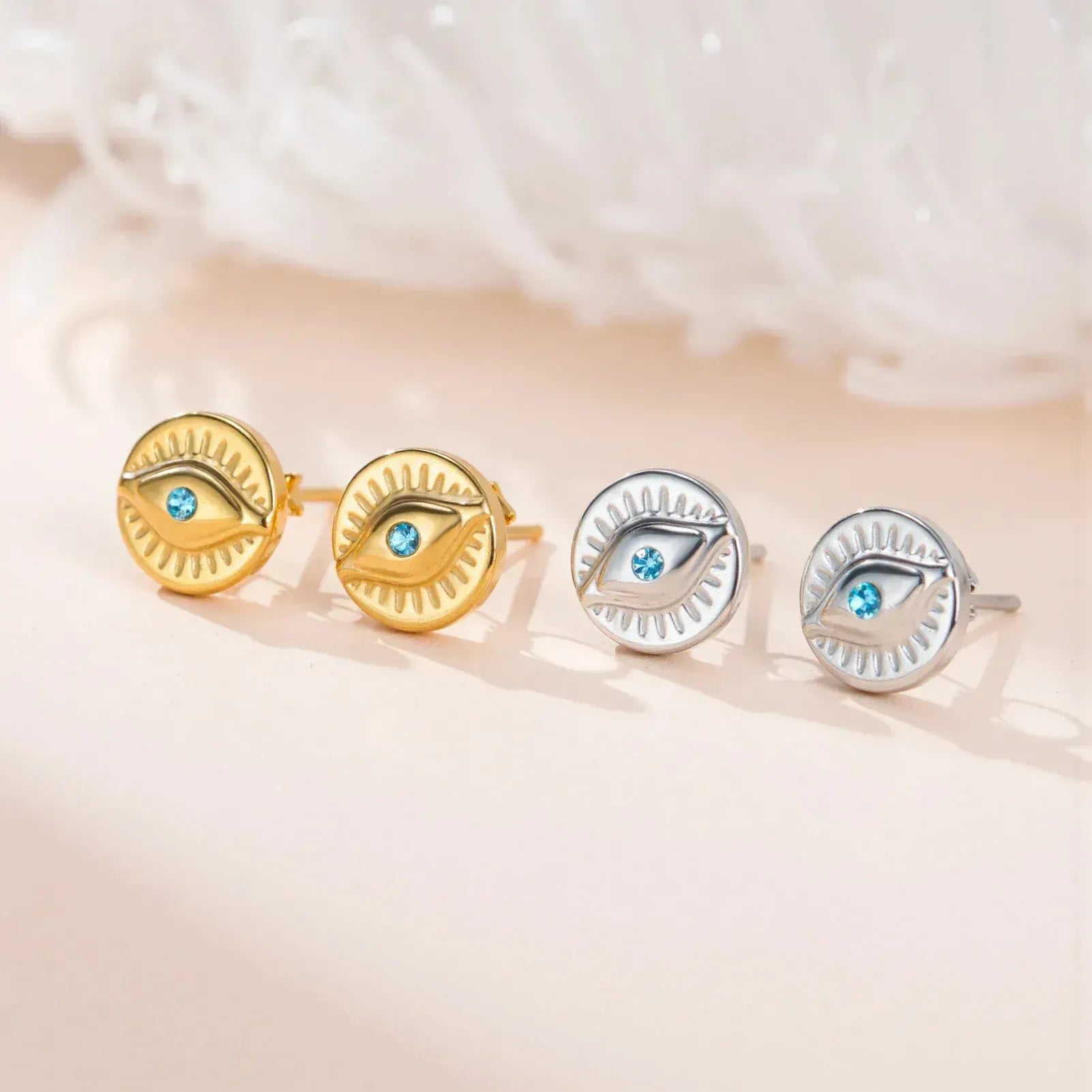 Pair of gold and silver eye-shaped earrings with gemstones on a soft beige background