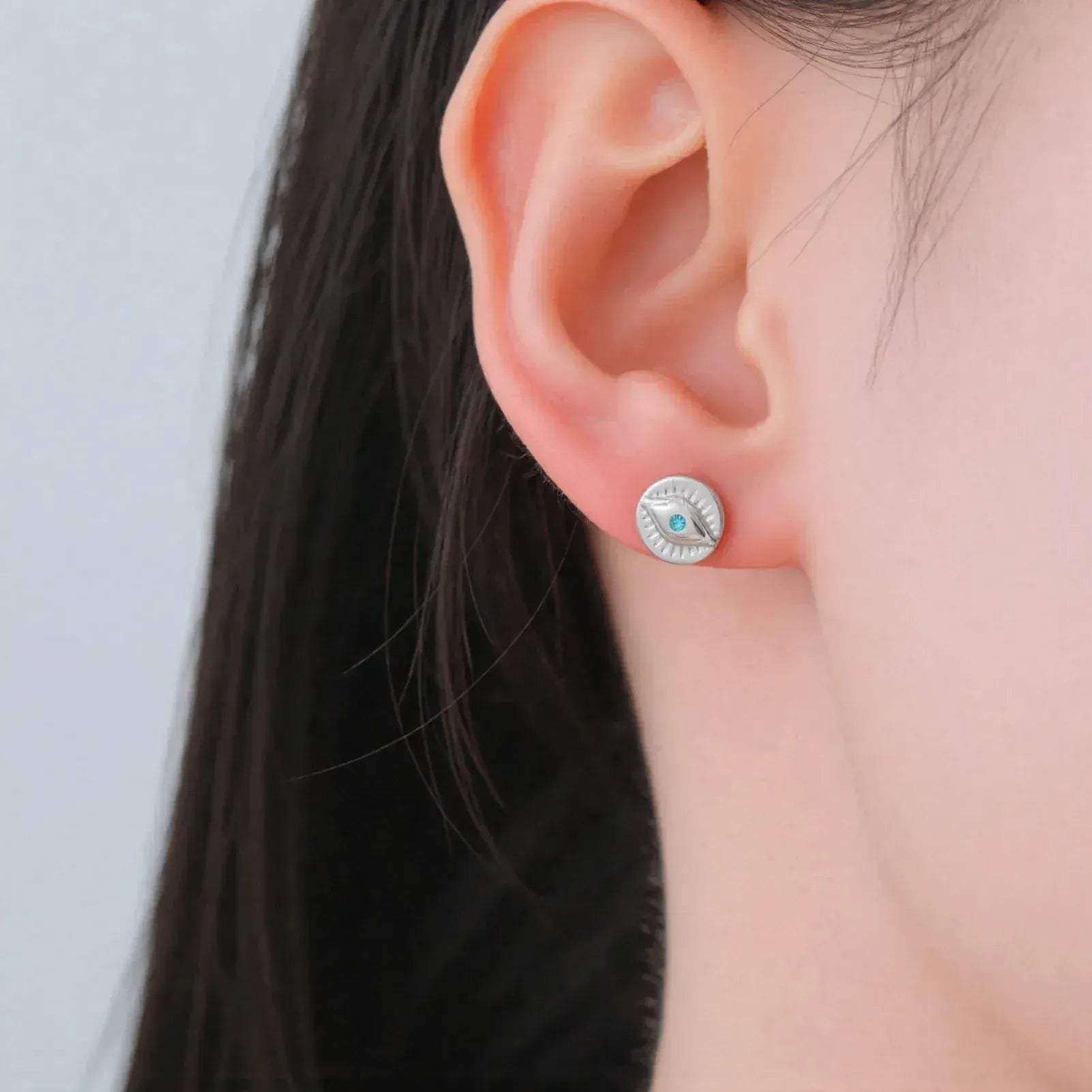 Silver earring with a blue gemstone worn by a person against a neutral background