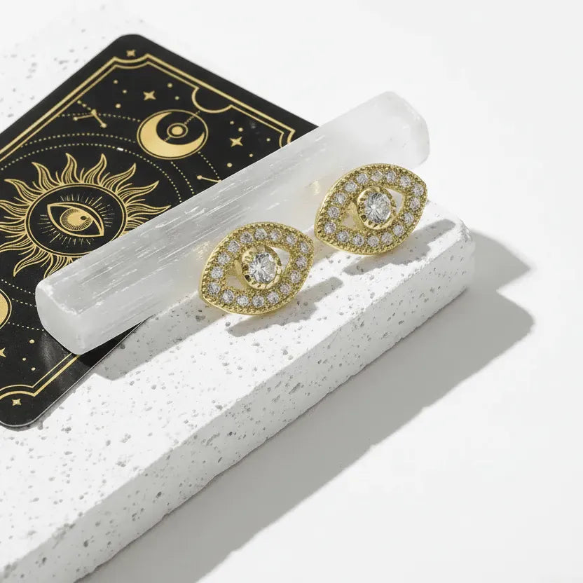 Gold earrings with gemstones on a white surface with a tarot card in the background