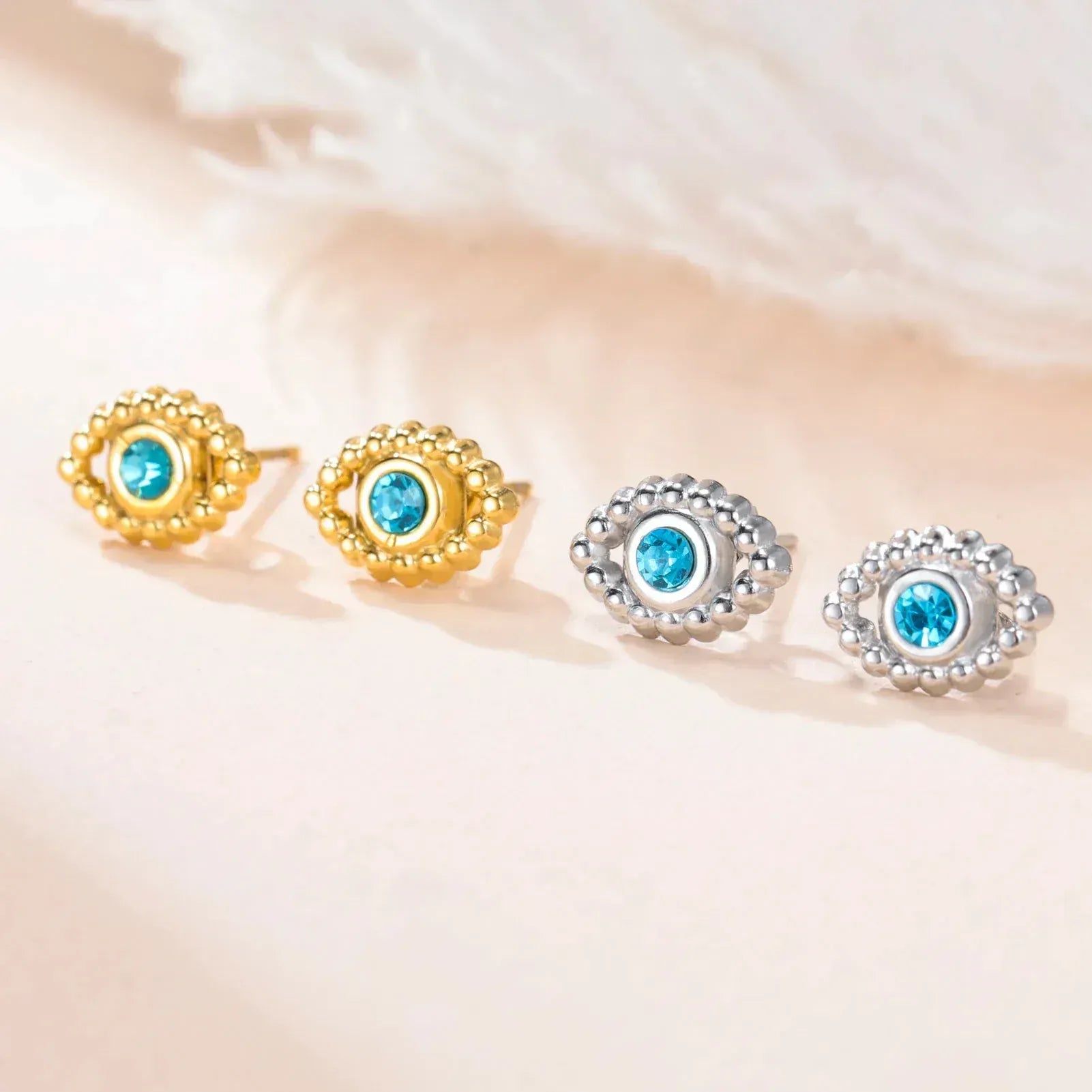 Pair of gold and silver earrings with blue gemstones on a soft beige background