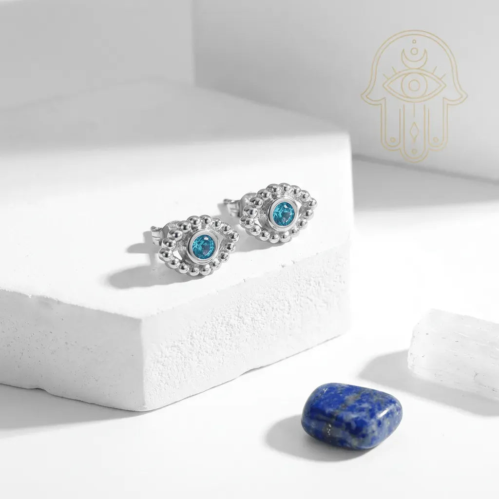 Silver earrings with blue gemstones on a white surface with a stone and logo in the background