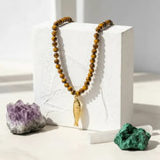 Beaded necklace with a gold fish pendant on a white block, surrounded by crystals.