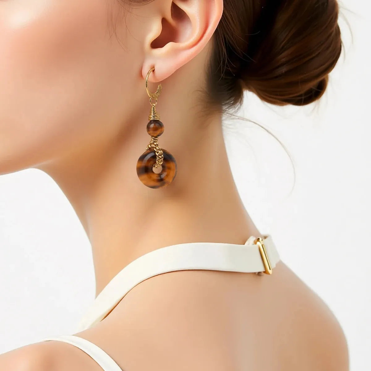 Close-up of a woman wearing tiger eye earrings with a white top.