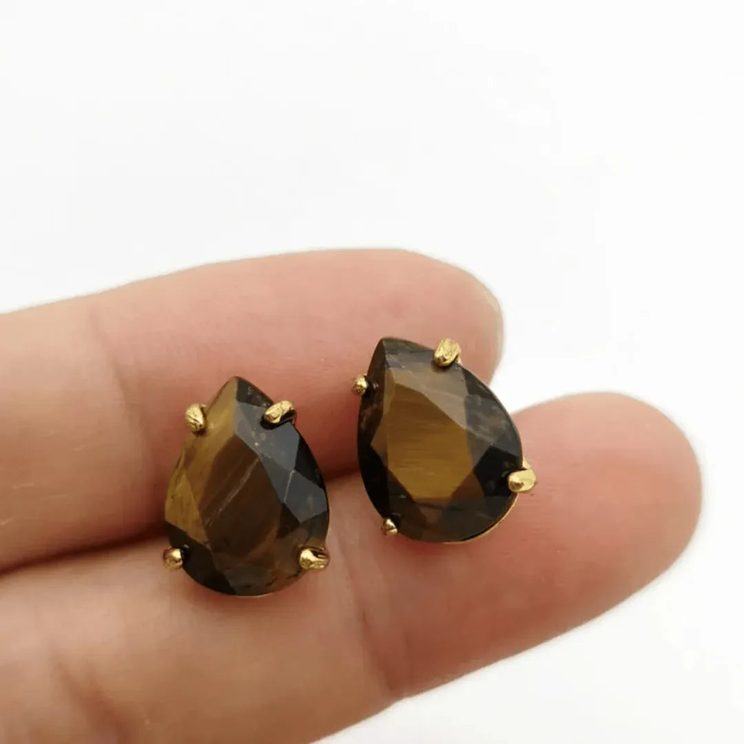Teardrop-shaped smoky brown gemstone earrings with gold posts on a finger against a white background