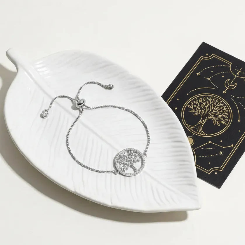 Silver Tree of Life bracelet on a white leaf-shaped dish with text about the bracelet's symbolism.