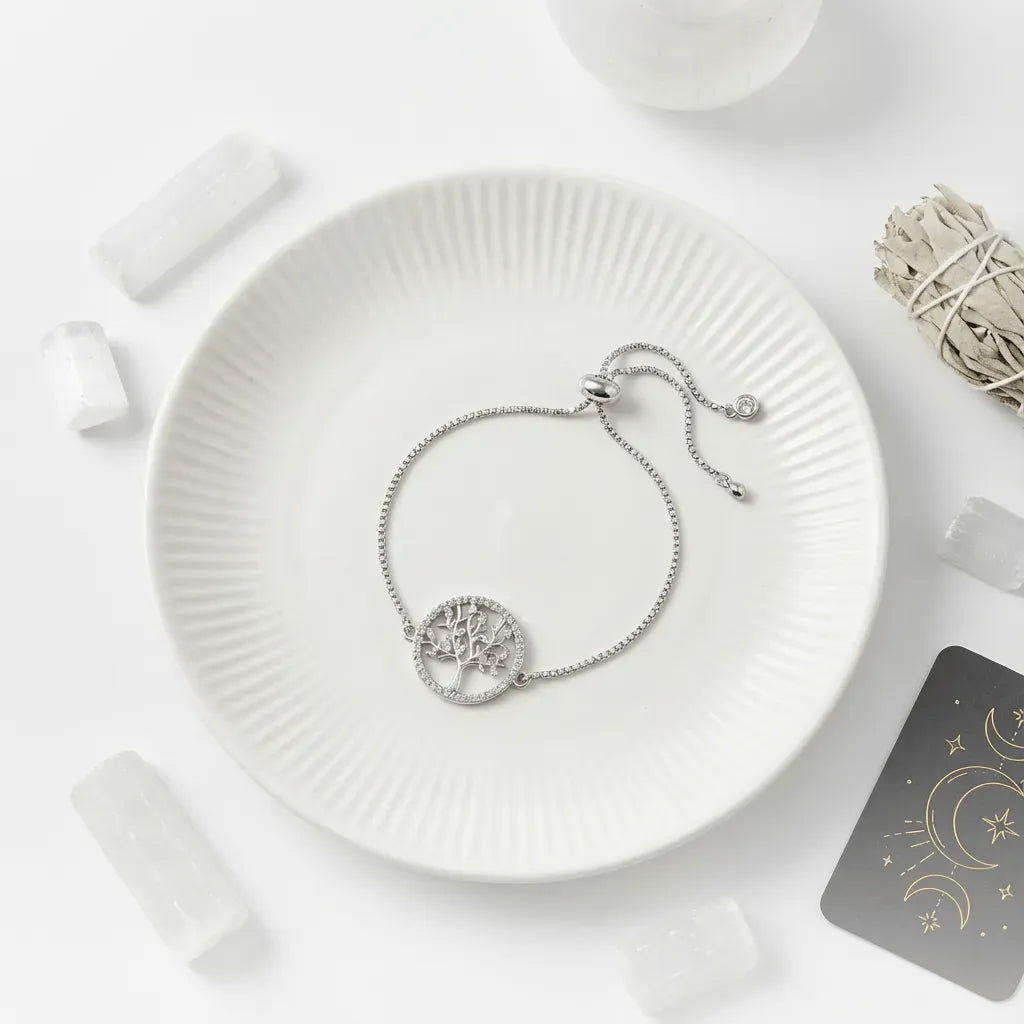Silver bracelet with tree of life design on a white plate, surrounded by minimal decor.