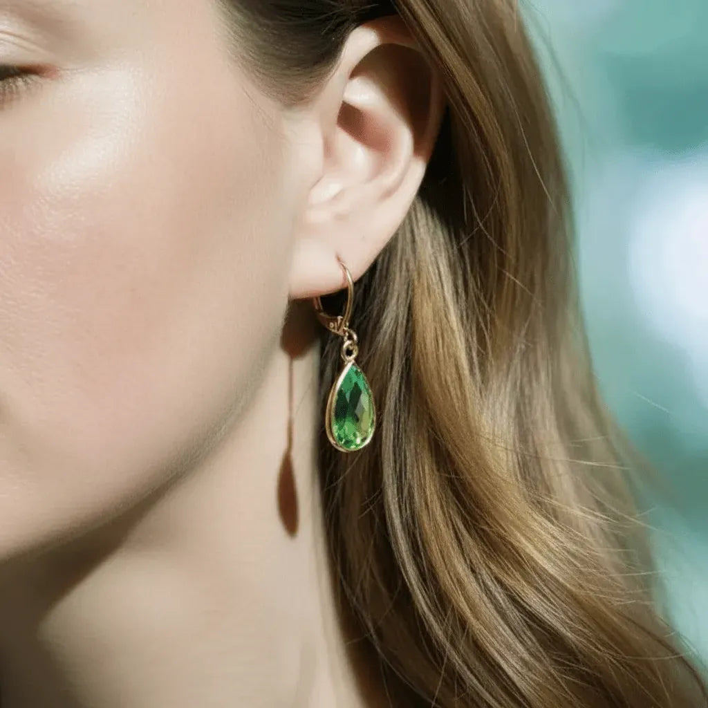 Close-up of a woman wearing a green teardrop earring with a blurred background