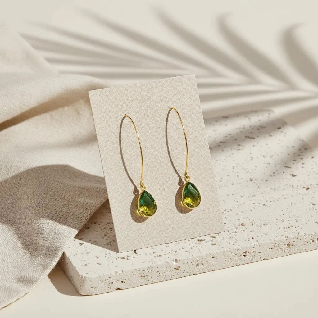 Green teardrop earrings on a beige card with a neutral background