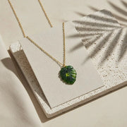 Gold necklace with a green leaf pendant on a textured beige surface