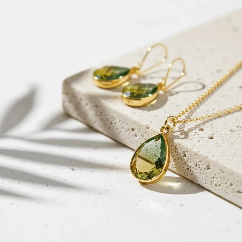 Gold necklace and earrings with green teardrop stones on a light surface