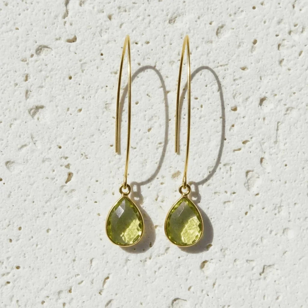 Gold earrings with green teardrop-shaped stones on a textured white background