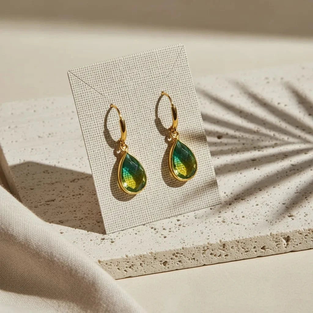 Gold and green teardrop earrings on a display card with a neutral background