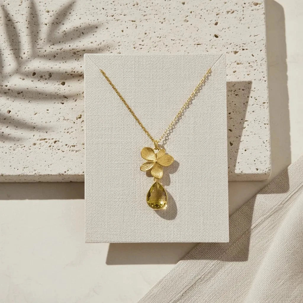 Gold necklace with a yellow pendant on a textured beige surface